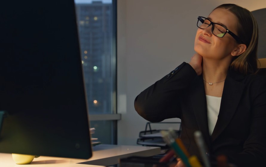 Woman experiencing neck pain while working late at night