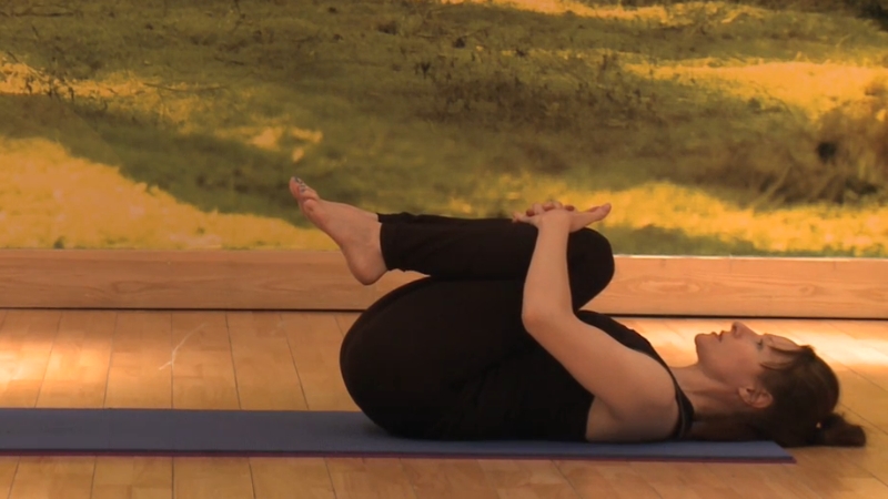 A woman practices Apanasana (Knees-to-Chest Pose) on a yoga mat