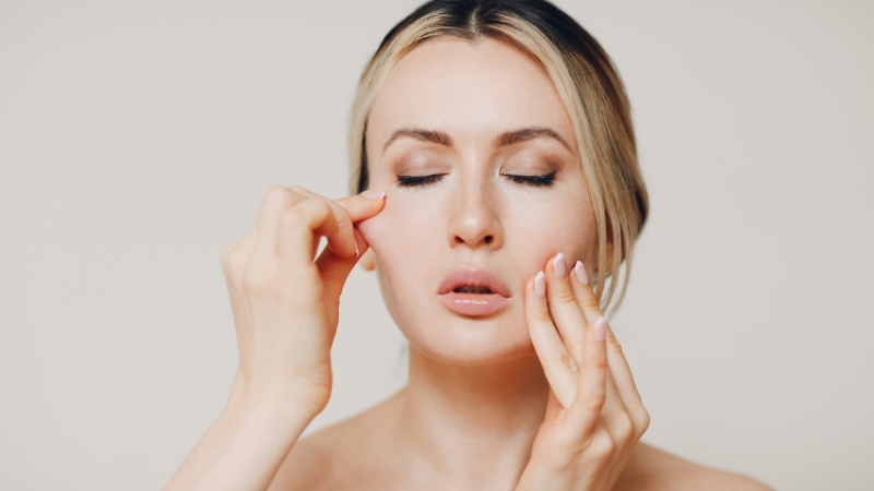Woman practicing face yoga by gently massaging her cheeks to reduce puffiness and improve circulation