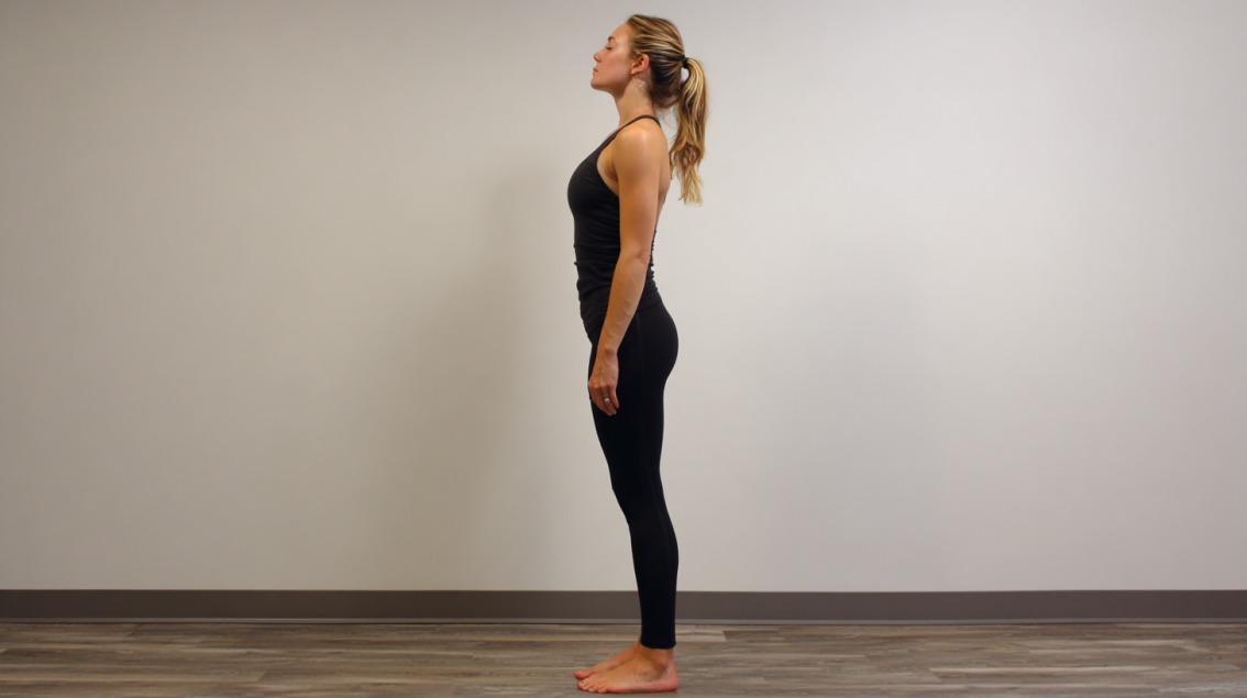 A woman practicing Mountain Pose (Tadasana), standing tall with feet together and arms at her sides