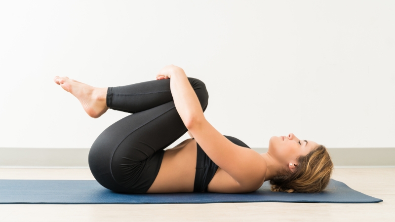 Woman practicing One-Leg Wind-Relieving Pose (Pavanamuktasana) on a yoga mat