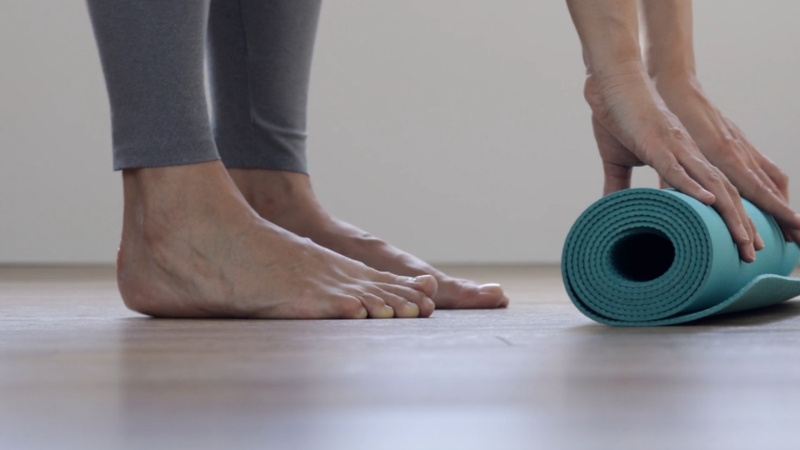 A person rolling out a yoga mat on the floor, preparing for a calming yoga session