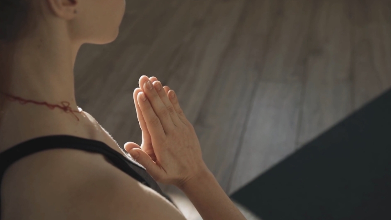 A woman sits on a yoga mat with hands in prayer position, preparing for yoga poses that help manage menstrual pain